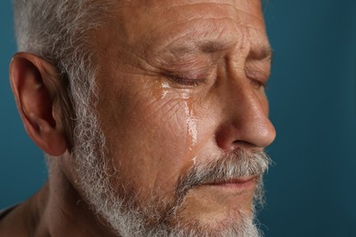 Photo of Sad senior man crying on blue background, closeup