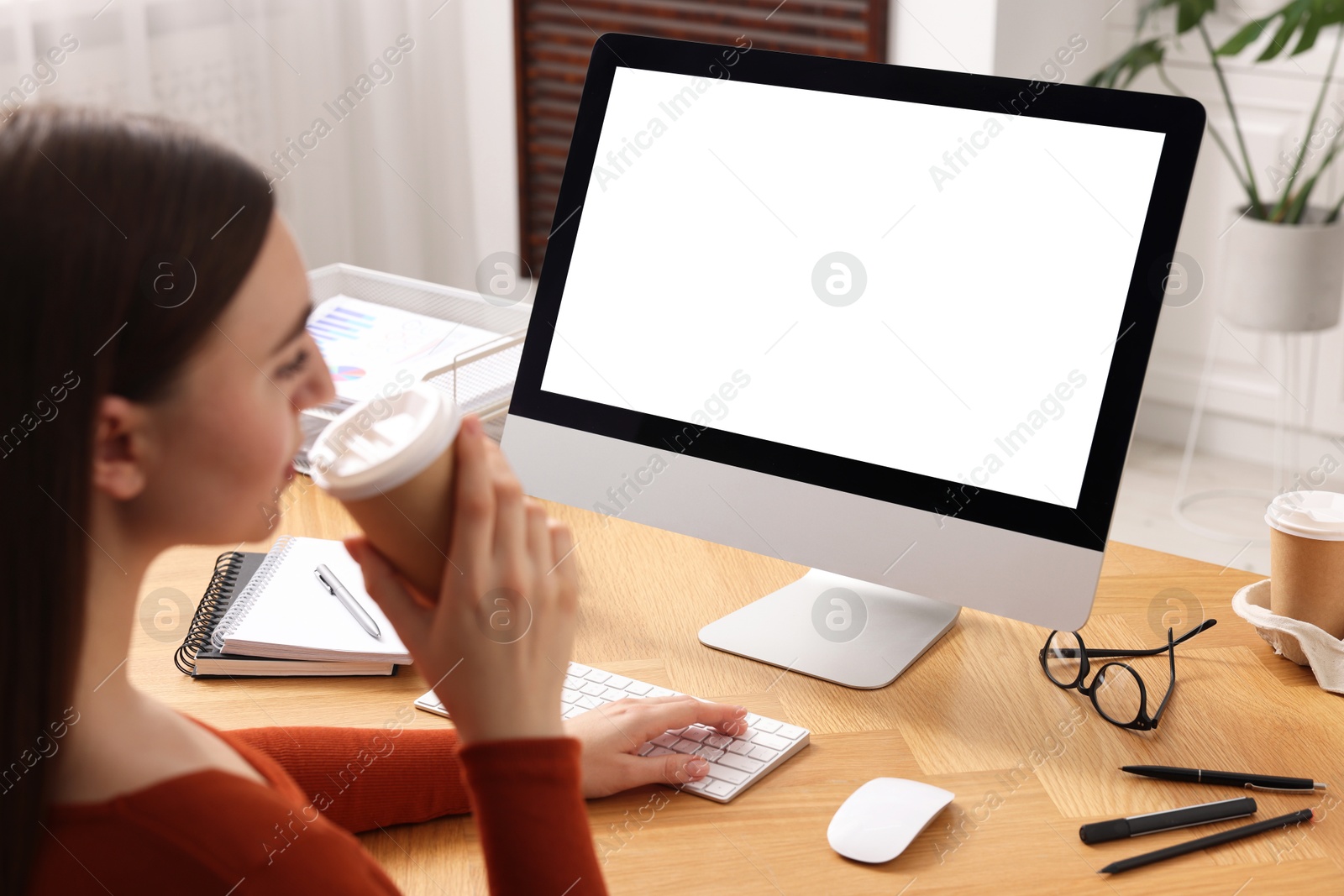 Photo of Woman with drink working on computer at wooden table in office