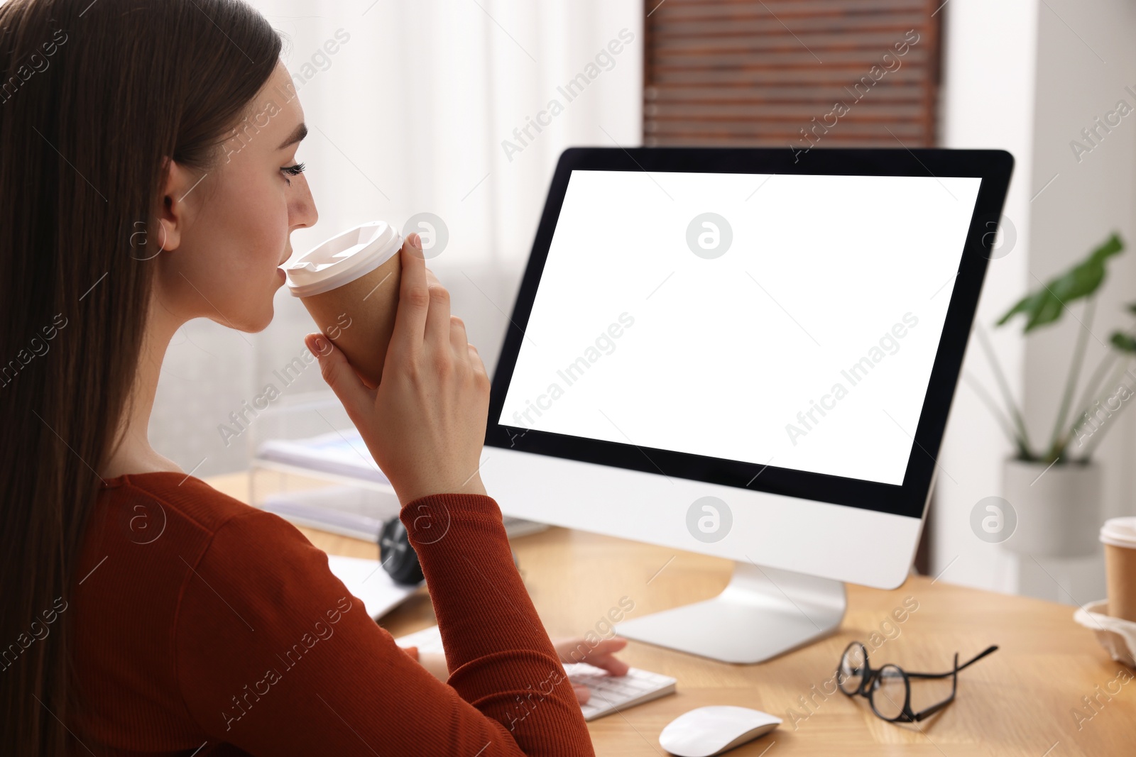 Photo of Woman with drink working on computer at wooden table in office