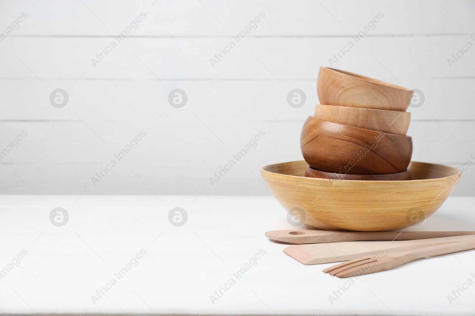 Photo of Wooden bowls and cooking utensils on white table, space for text