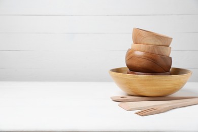 Photo of Wooden bowls and cooking utensils on white table, space for text