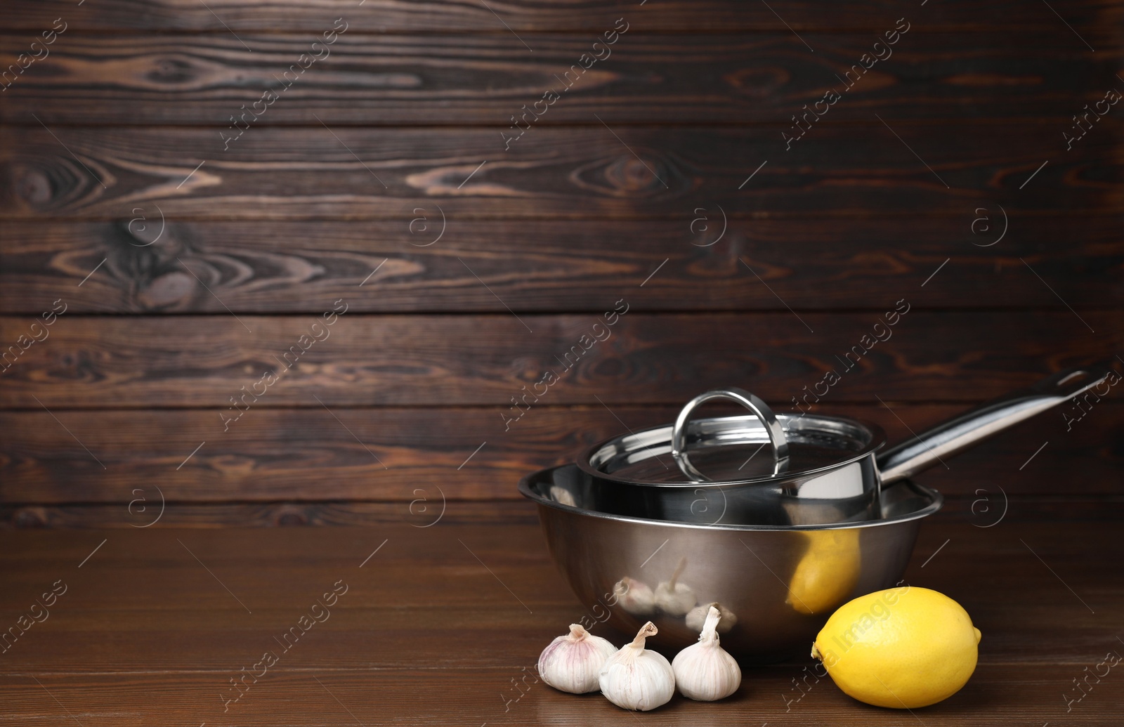 Photo of Bowl, saucepan, lemon and garlic on wooden table, space for text. Cooking utensils