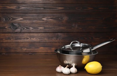 Photo of Bowl, saucepan, lemon and garlic on wooden table, space for text. Cooking utensils