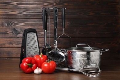 Photo of Dishware and cooking utensils with vegetables on wooden table