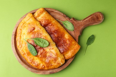 Photo of Tasty calzones with basil on green background, top view