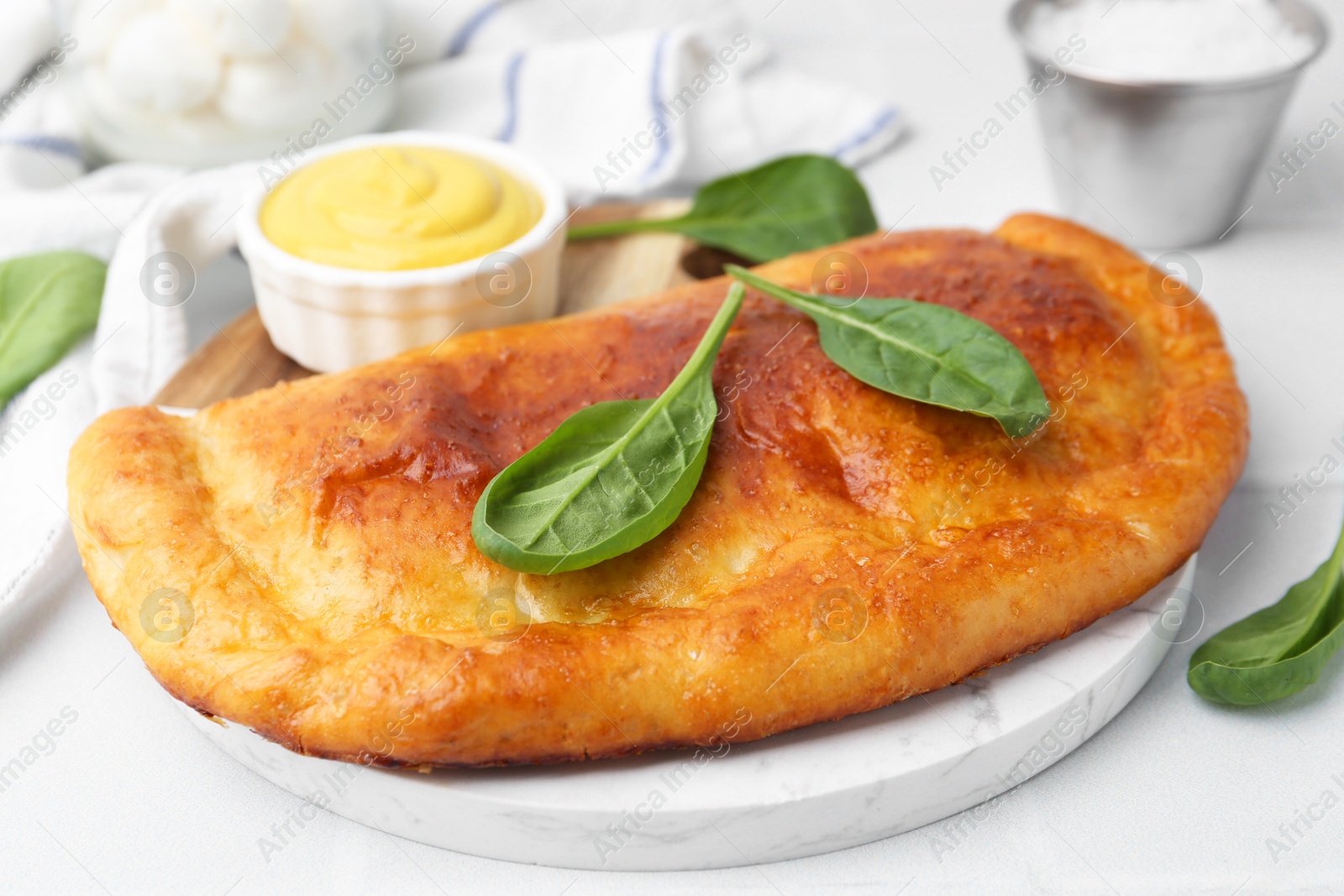 Photo of Tasty calzone with basil and sauce on white table, closeup