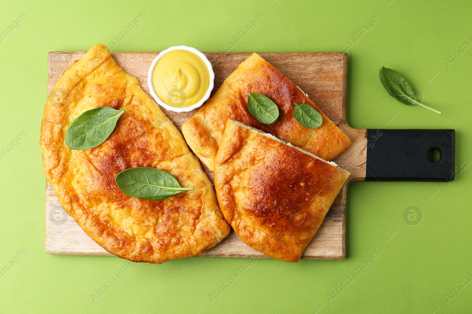 Photo of Tasty calzones with basil and sauce on green background, top view