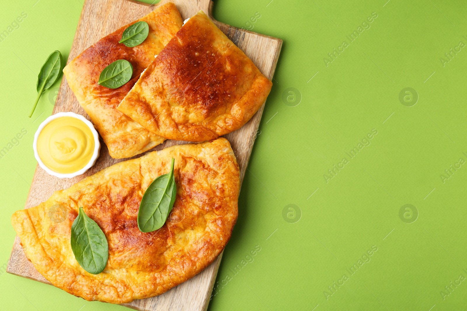 Photo of Tasty calzones with basil and sauce on green background, top view. Space for text