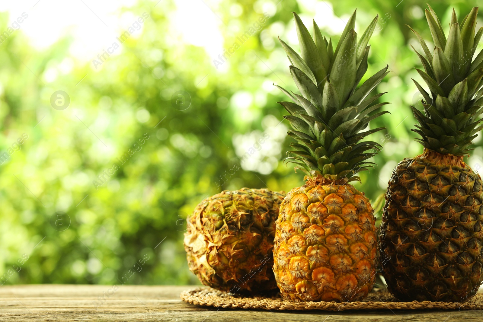 Photo of Fresh ripe pineapples on wooden table against blurred background, space for text