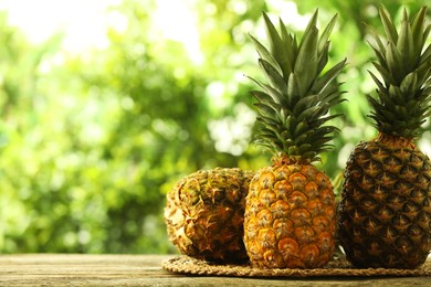 Photo of Fresh ripe pineapples on wooden table against blurred background, space for text