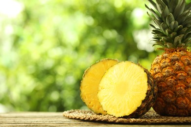 Photo of Fresh ripe pineapples on wooden table against blurred background, closeup. Space for text