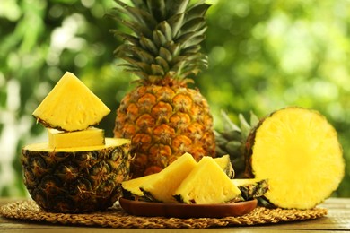 Photo of Fresh ripe pineapples on wooden table against blurred background