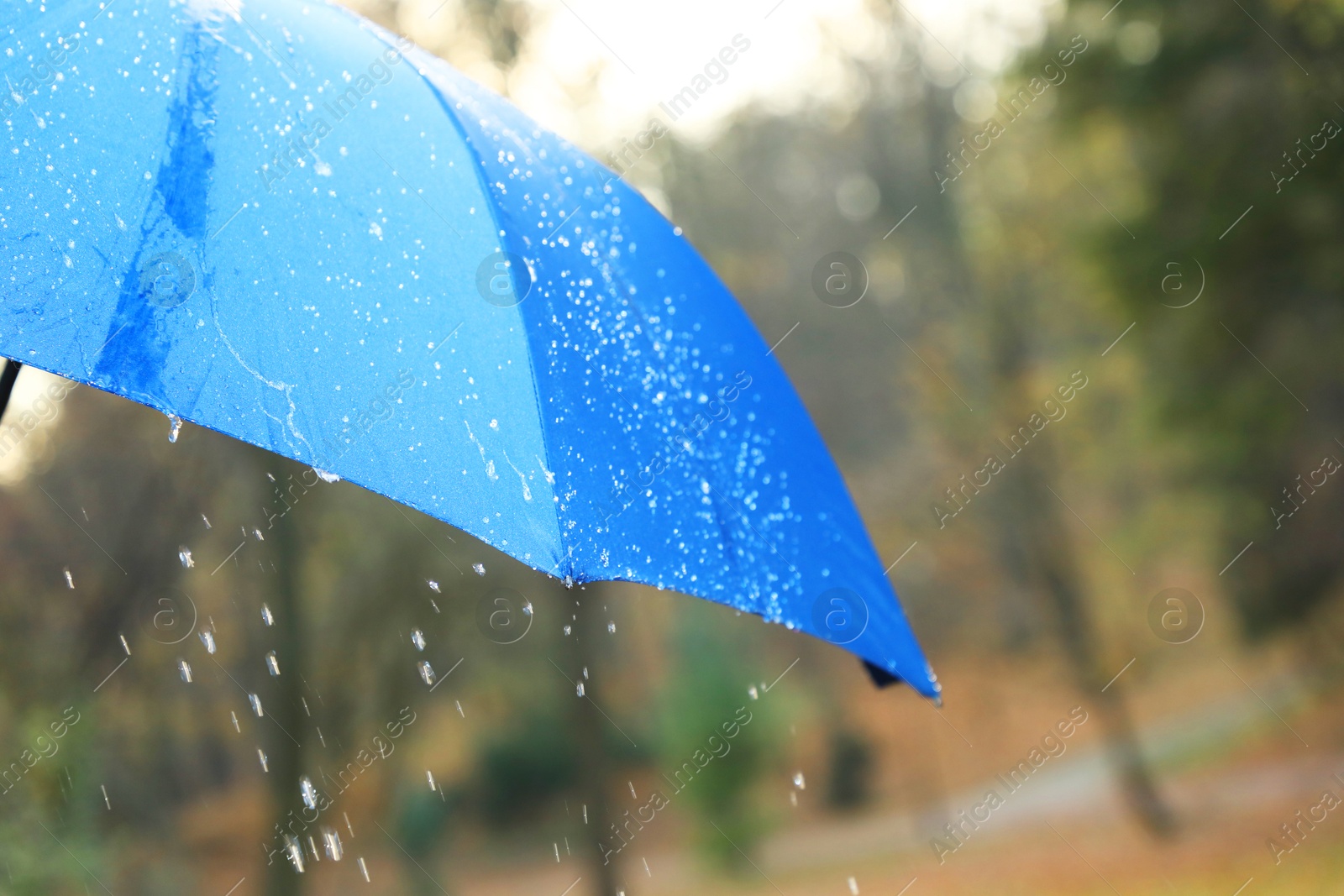 Photo of Open blue umbrella under pouring rain outdoors, closeup. Space for text