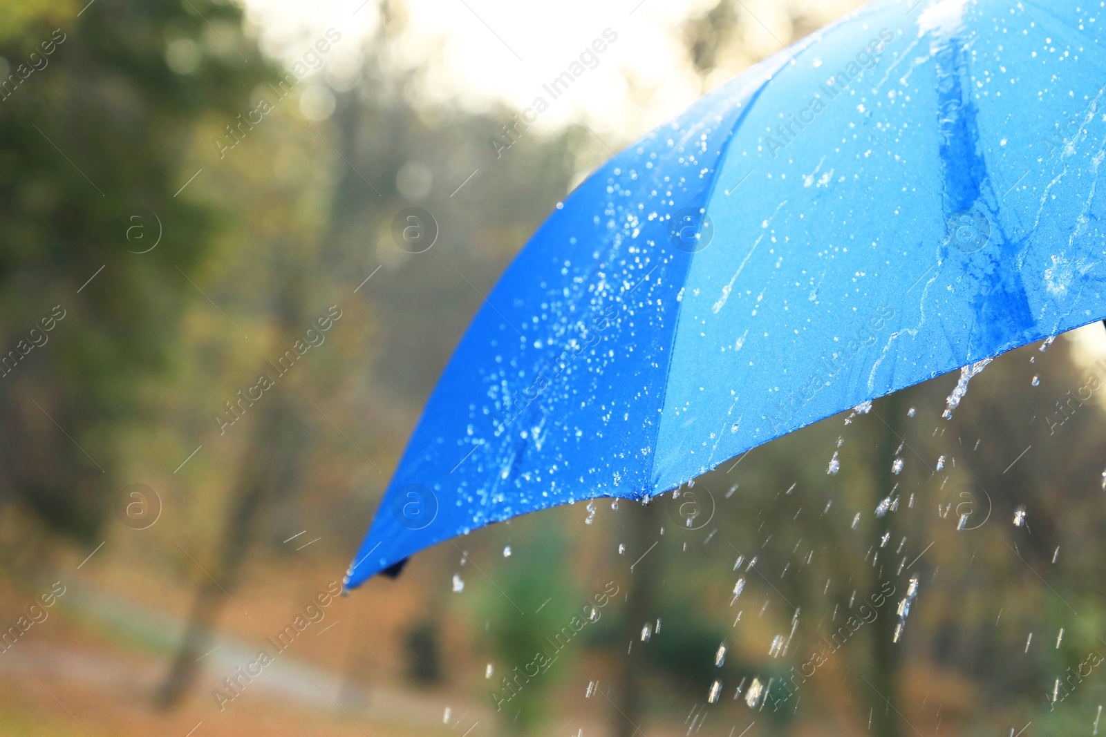 Photo of Open blue umbrella under pouring rain outdoors, closeup. Space for text