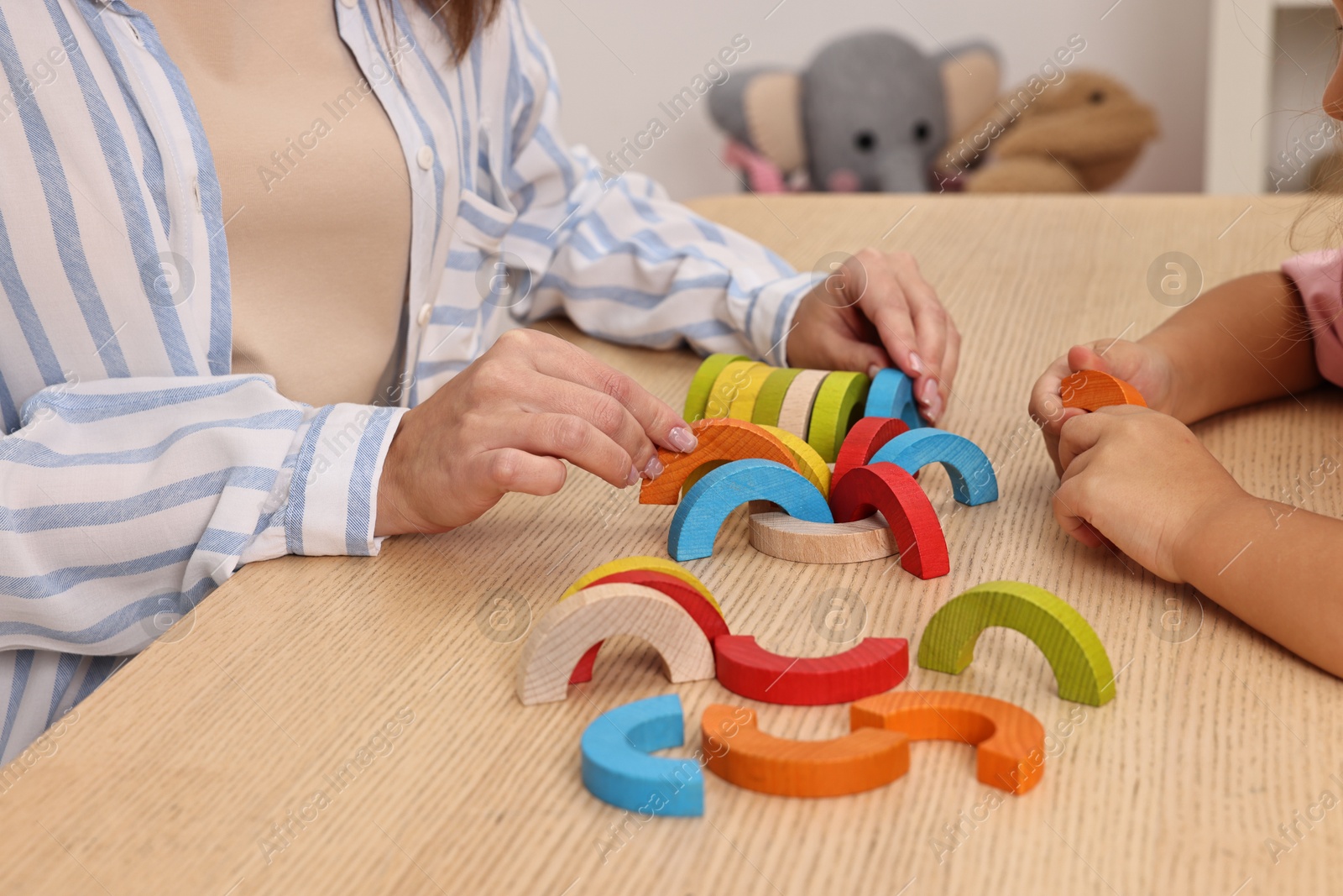 Photo of Autism therapy. Psychologist and little girl playing with educational toy at wooden table, closeup