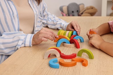 Photo of Autism therapy. Psychologist and little girl playing with educational toy at wooden table, closeup