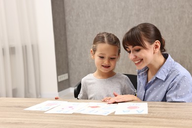 Photo of Smiling speech therapist working with little girl at table in autism treatment center. Space for text