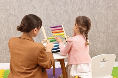 Photo of Autism therapy. Psychologist and little girl playing with wooden abacus indoors, back view