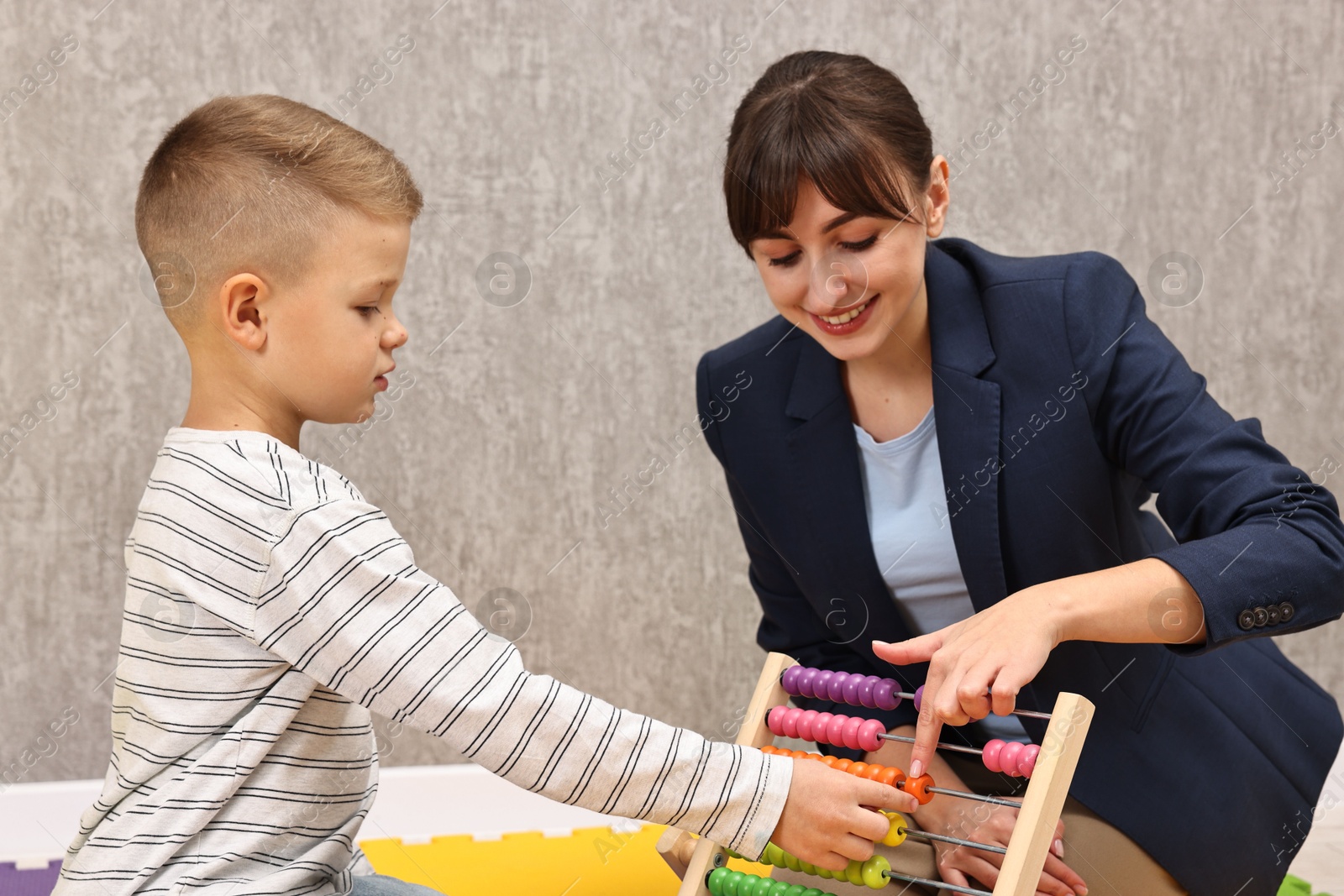 Photo of Autism therapy. Smiling psychologist and little boy playing with abacus in mental health center