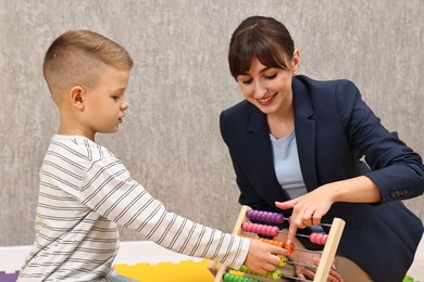 Photo of Autism therapy. Smiling psychologist and little boy playing with abacus in mental health center