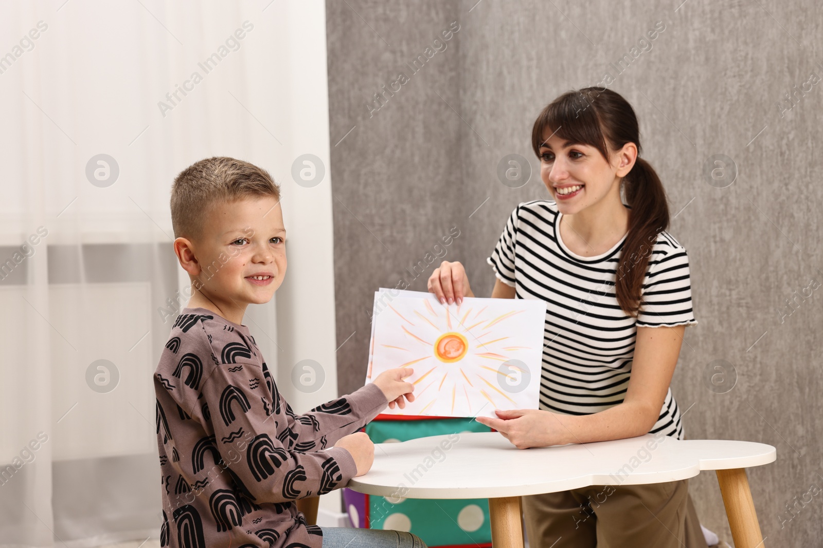 Photo of Autism therapy. Smiling psychologist working with little boy at table in mental health center