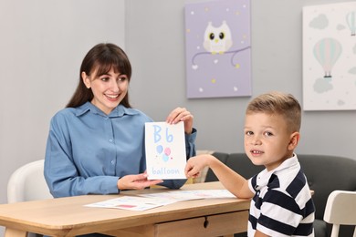 Photo of Smiling speech therapist working with little boy at table in autism treatment center