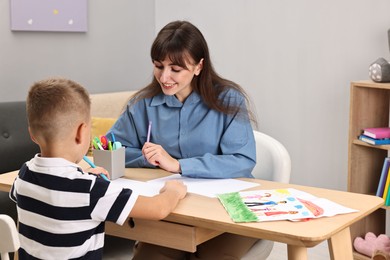 Photo of Autism therapy. Smiling psychologist and little boy drawing pictures at table in mental health center