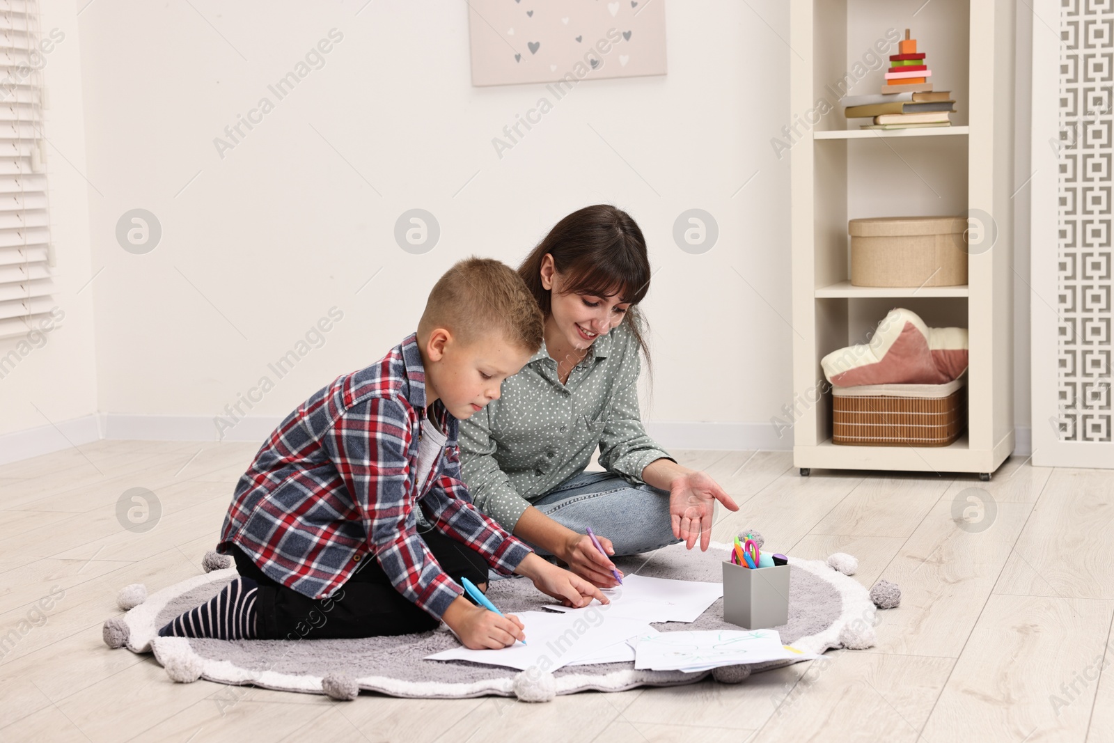 Photo of Autism therapy. Smiling psychologist and little boy drawing pictures in mental health center