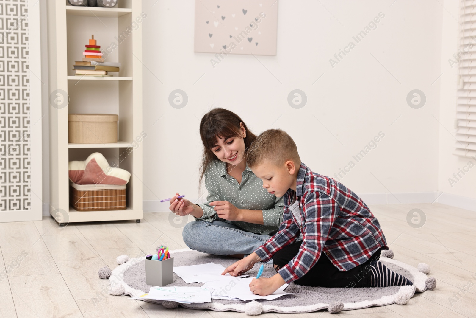 Photo of Autism therapy. Smiling psychologist and little boy drawing pictures in mental health center