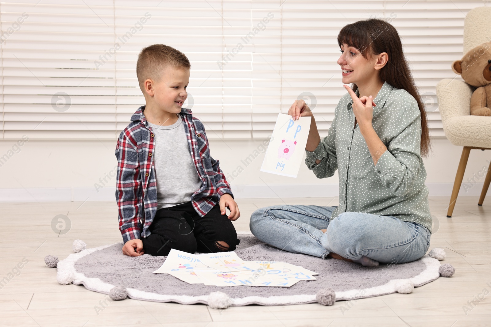 Photo of Smiling speech therapist working with little boy on floor in autism treatment center