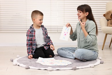 Photo of Smiling speech therapist working with little boy on floor in autism treatment center