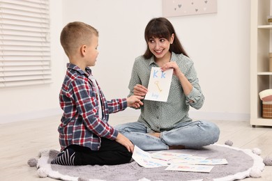 Photo of Smiling speech therapist working with little boy on floor in autism treatment center