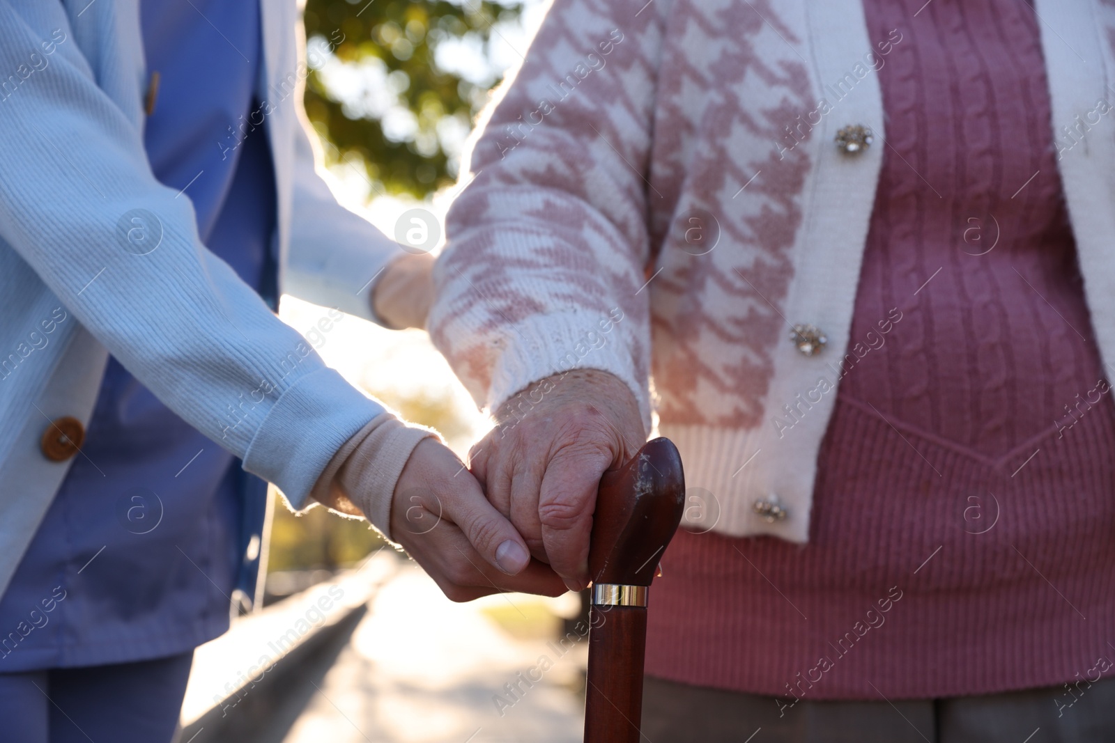 Photo of Elderly woman with walking cane and her caregiver in park, closeup