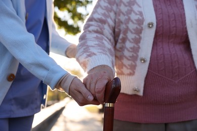 Photo of Elderly woman with walking cane and her caregiver in park, closeup