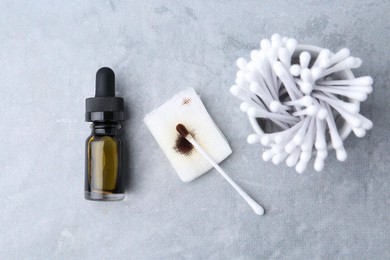 Photo of Bottle of iodine with dropper, piece of bandage and cotton swabs on grey table, flat lay