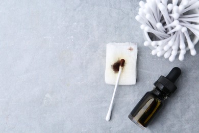 Photo of Bottle of iodine with dropper, piece of bandage and cotton swabs on grey table, flat lay. Space for text