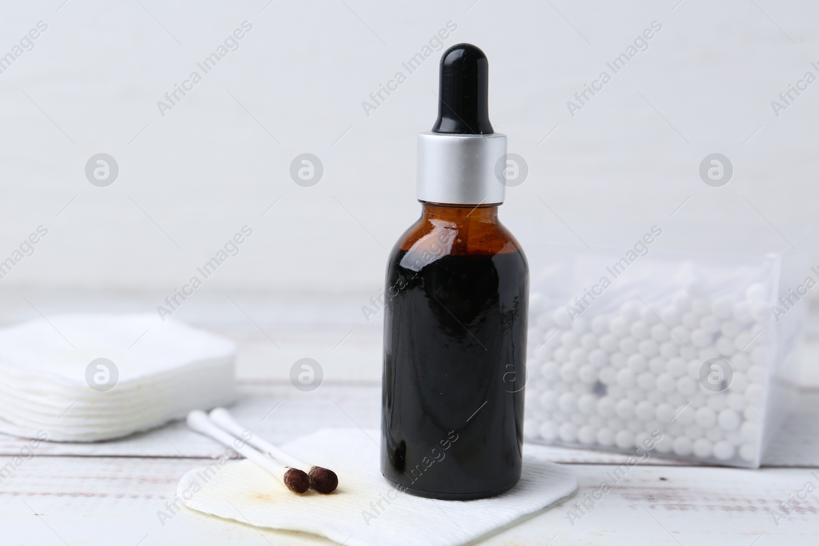 Photo of Bottle of iodine with dropper, cotton pads and swabs on white wooden table, closeup