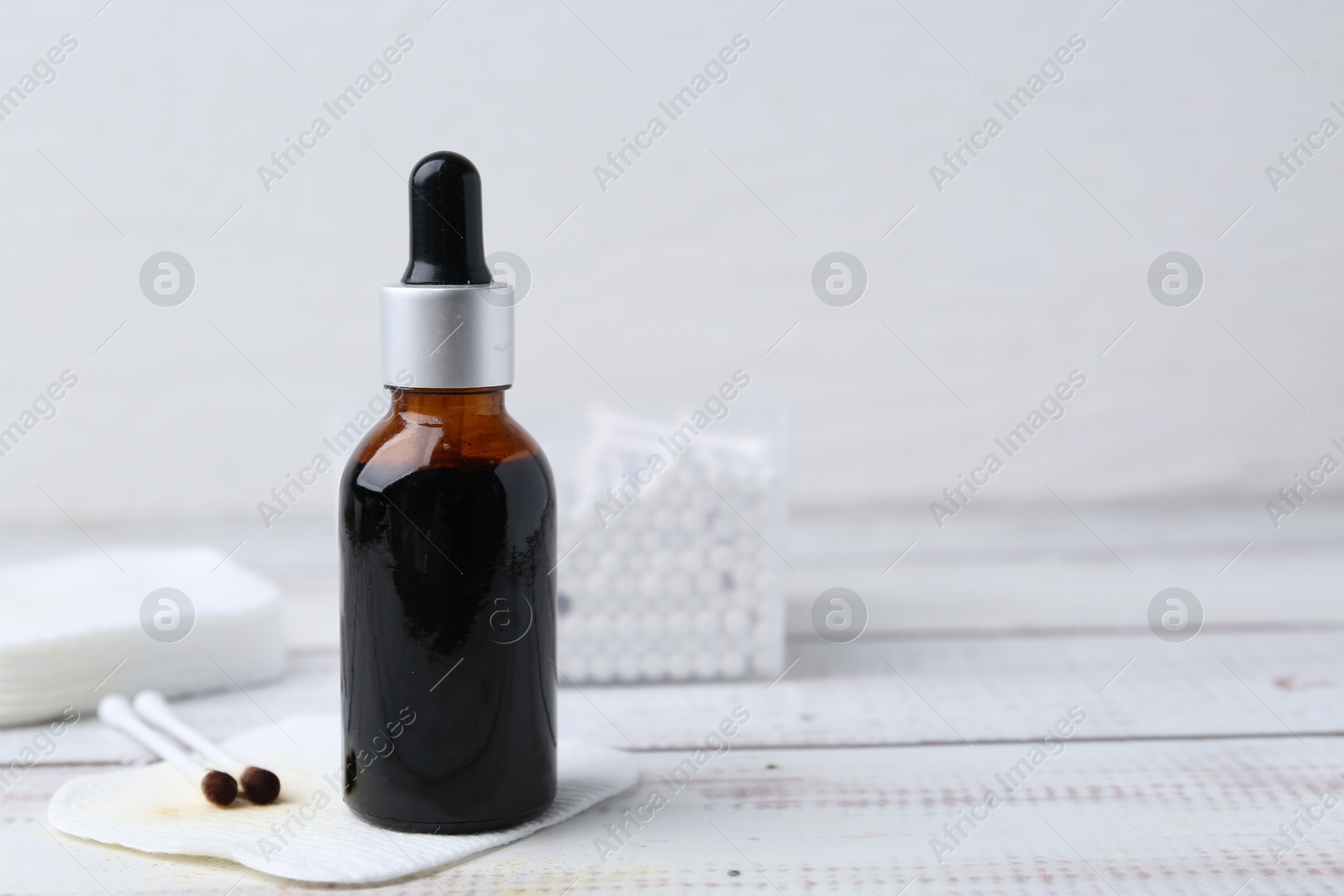 Photo of Bottle of iodine with dropper, cotton pads and swabs on white wooden table, closeup. Space for text