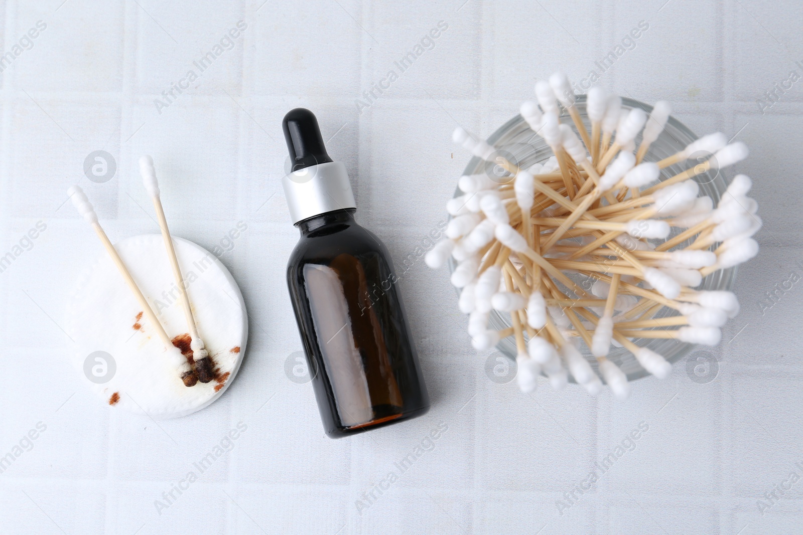 Photo of Bottle of iodine with dropper, cotton pads and swabs on white tiled table, flat lay