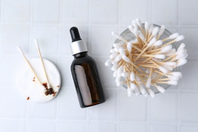 Photo of Bottle of iodine with dropper, cotton pads and swabs on white tiled table, flat lay