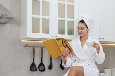 Spa day. Beautiful woman with face mask and cup of drink reading magazine in kitchen