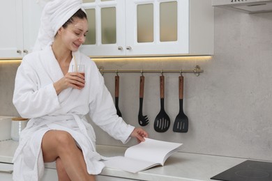 Spa day. Beautiful woman with face mask and glass of juice reading magazine in kitchen