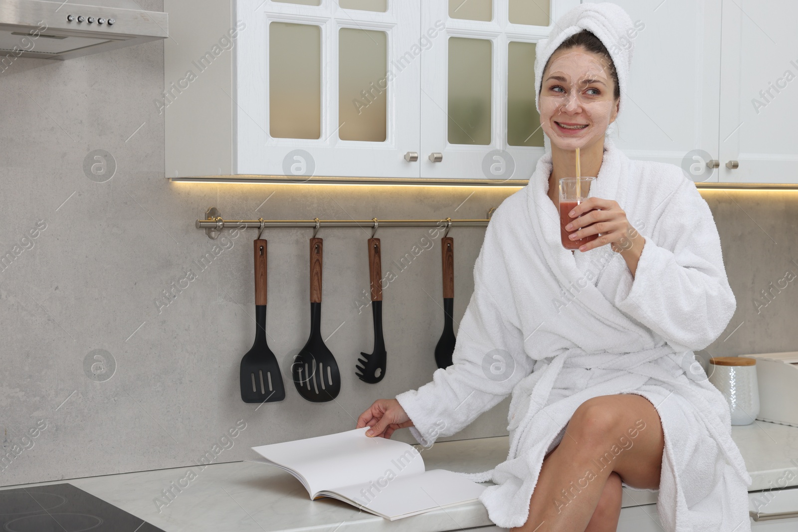 Photo of Spa day. Beautiful woman with face mask and glass of juice reading magazine in kitchen