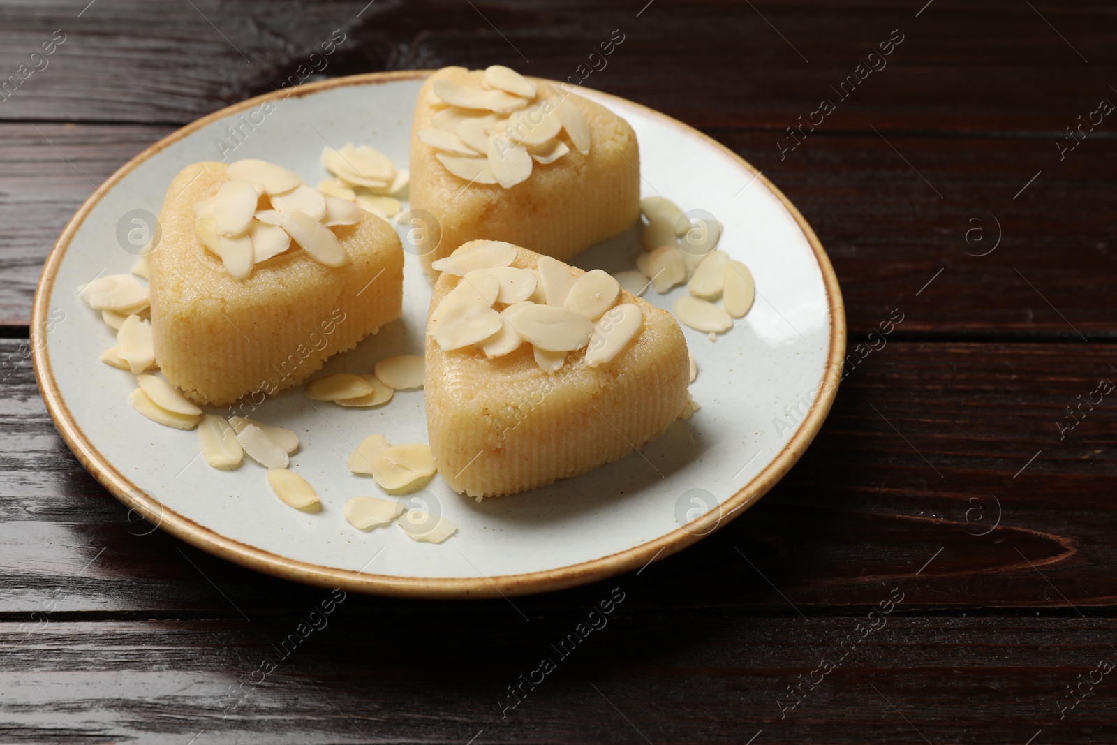 Photo of Pieces of delicious semolina halva with almond flakes on wooden table