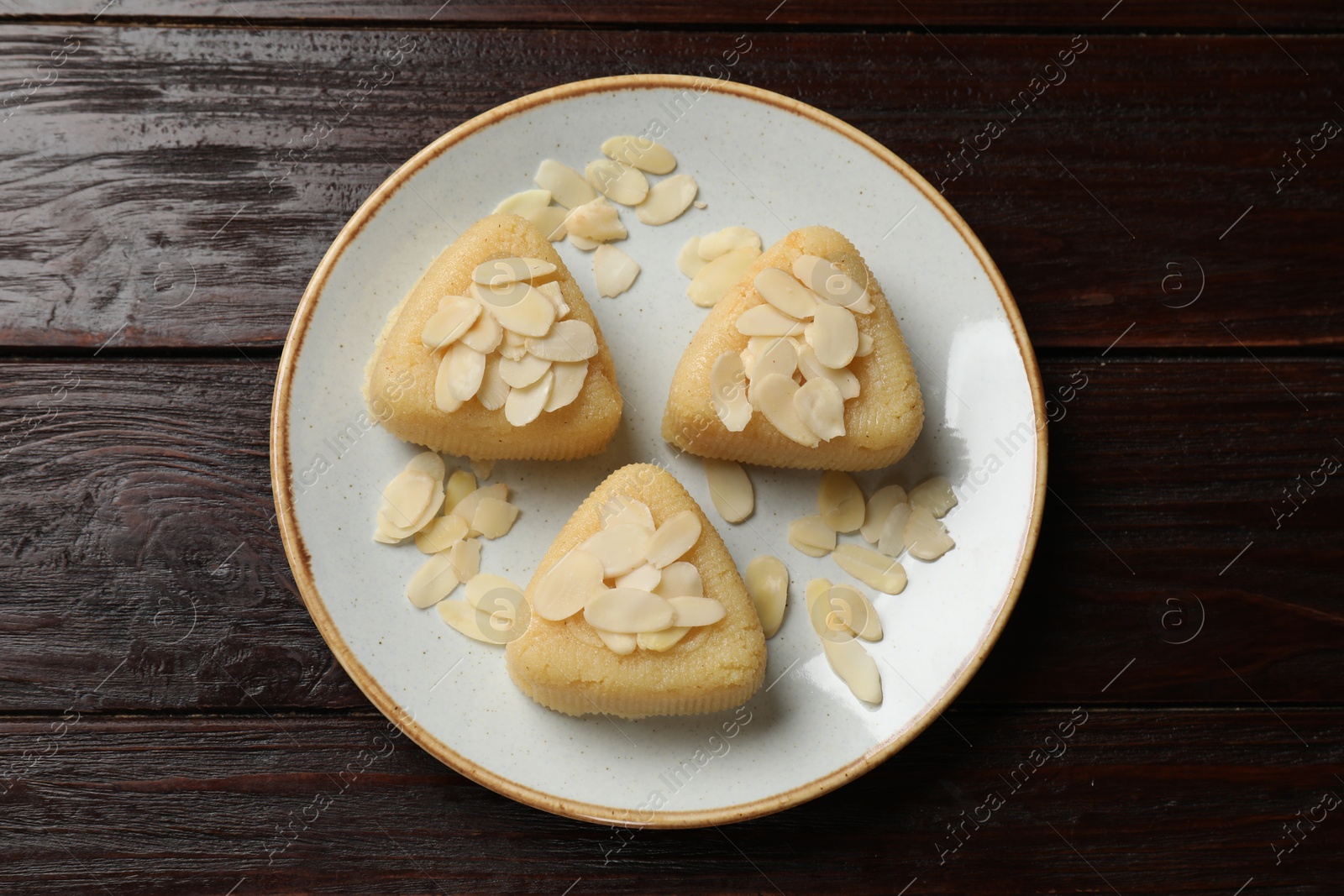 Photo of Pieces of delicious semolina halva with almond flakes on wooden table, top view