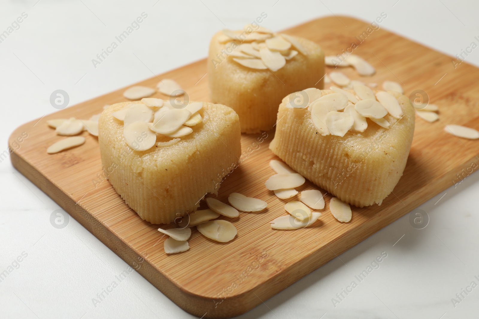 Photo of Pieces of delicious semolina halva with almond flakes on white table, closeup