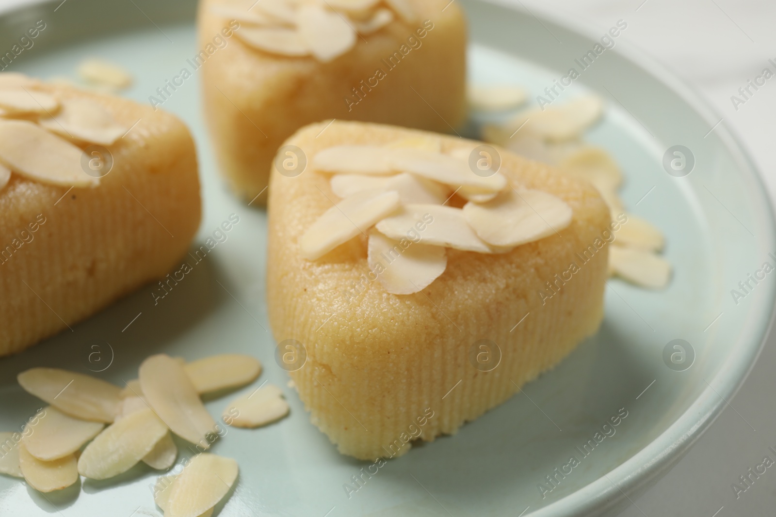 Photo of Pieces of delicious semolina halva with almond flakes on white table, closeup