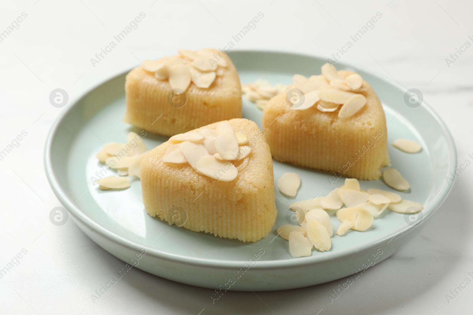 Photo of Pieces of delicious semolina halva with almond flakes on white marble table, closeup