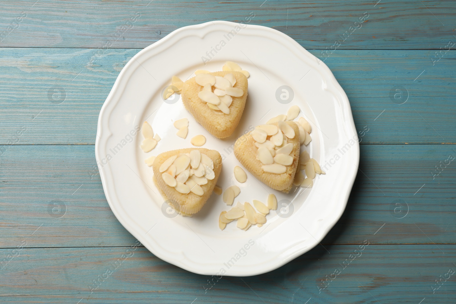 Photo of Pieces of delicious sweet semolina halva with almond flakes on blue wooden table, top view