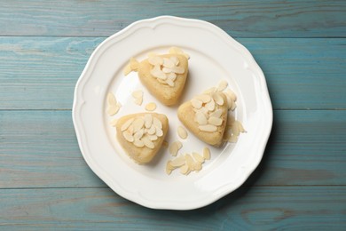 Photo of Pieces of delicious sweet semolina halva with almond flakes on blue wooden table, top view